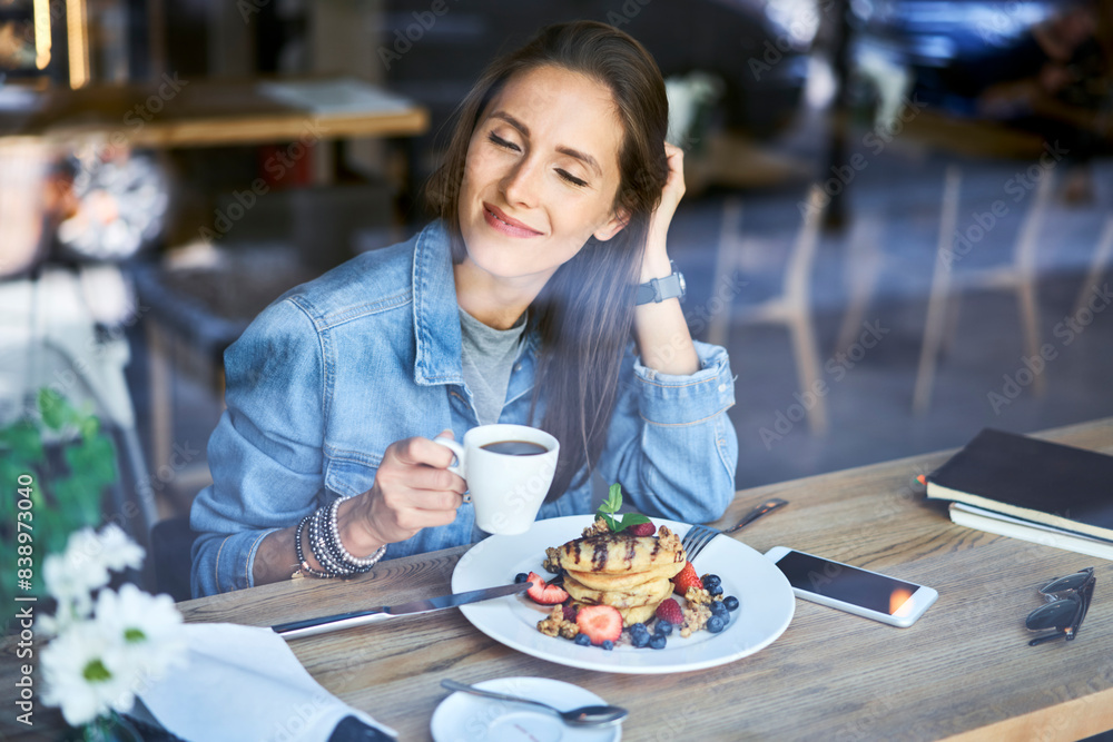 Smiling young woman enjoying pancakes and coffee in cafe Smiling young woman enjoying pancakes and coffee in cafe