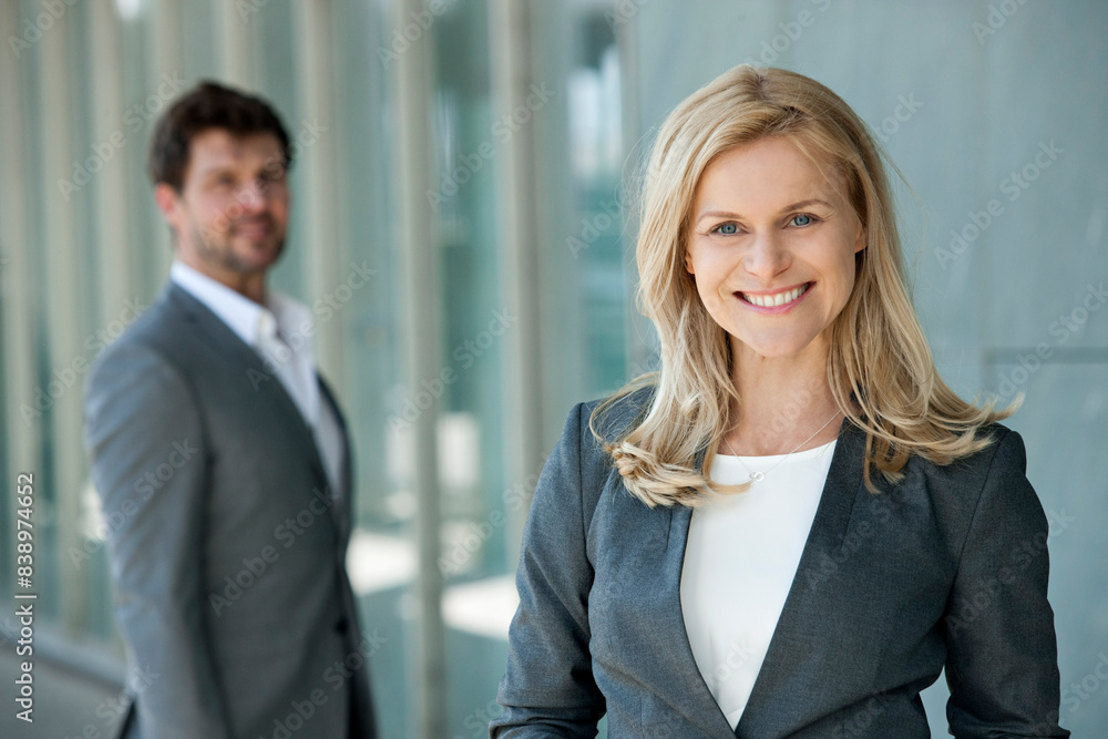 Portrait of smiling businesswoman with her partner watching in the background Portrait of smiling businesswoman with her partner watching in the background