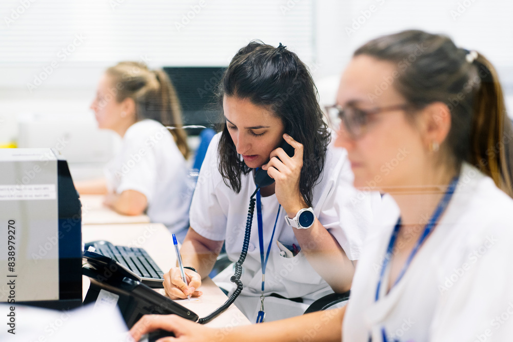 Female pharmacist writing while talking over telephone at desk in hospital