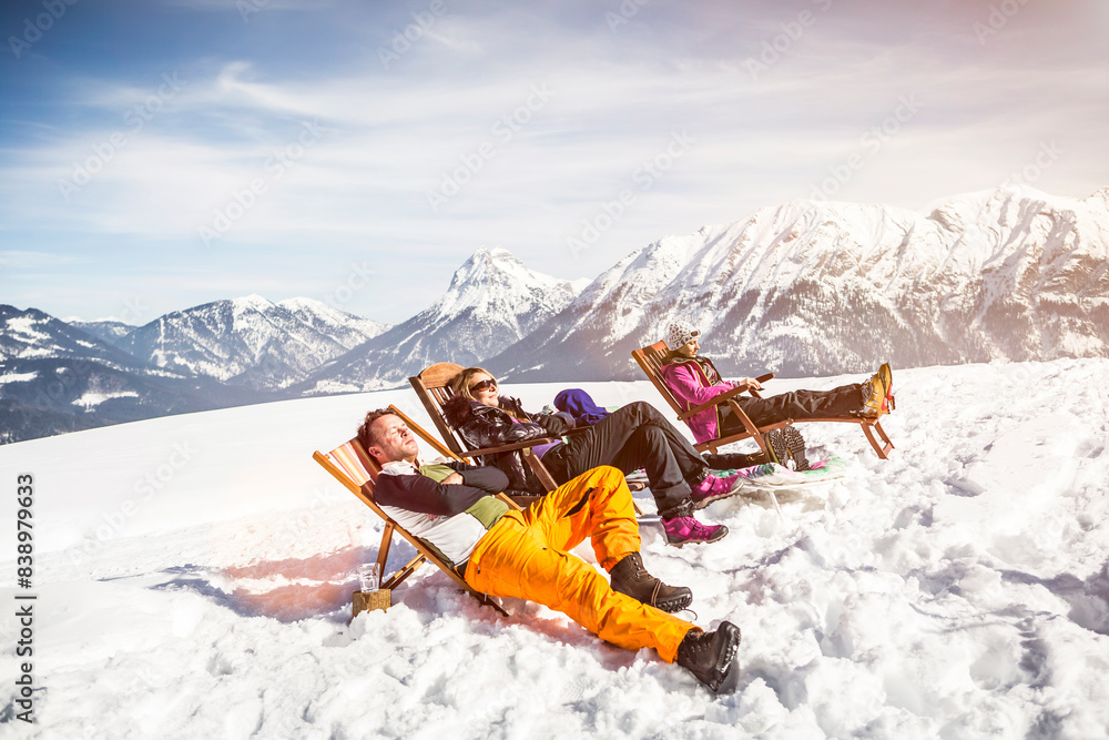 Friends sunbathing in deck chairs in mountainscape in winter, Achenkirch, Austria