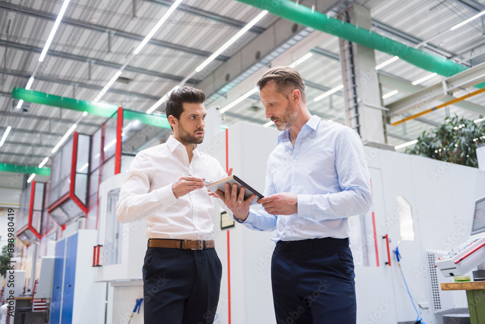 Two businessmen with tablet in factory shop floor discussing Two businessmen with tablet in factory shop floor discussing