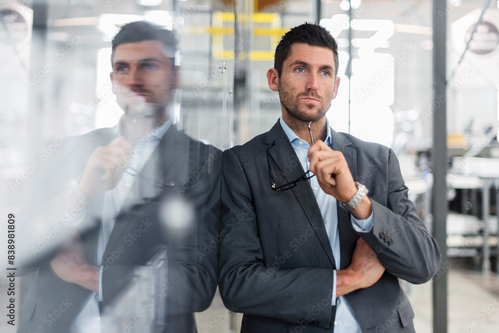 Businessman leaning against glass pane in modern factory thinking Businessman leaning against glass pane in modern factory thinking