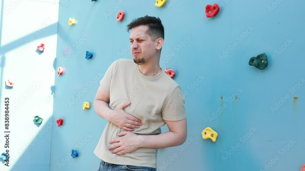 Man Holding Stomach in Front of Climbing Wall Man Holding Stomach in Front of Climbing Wall