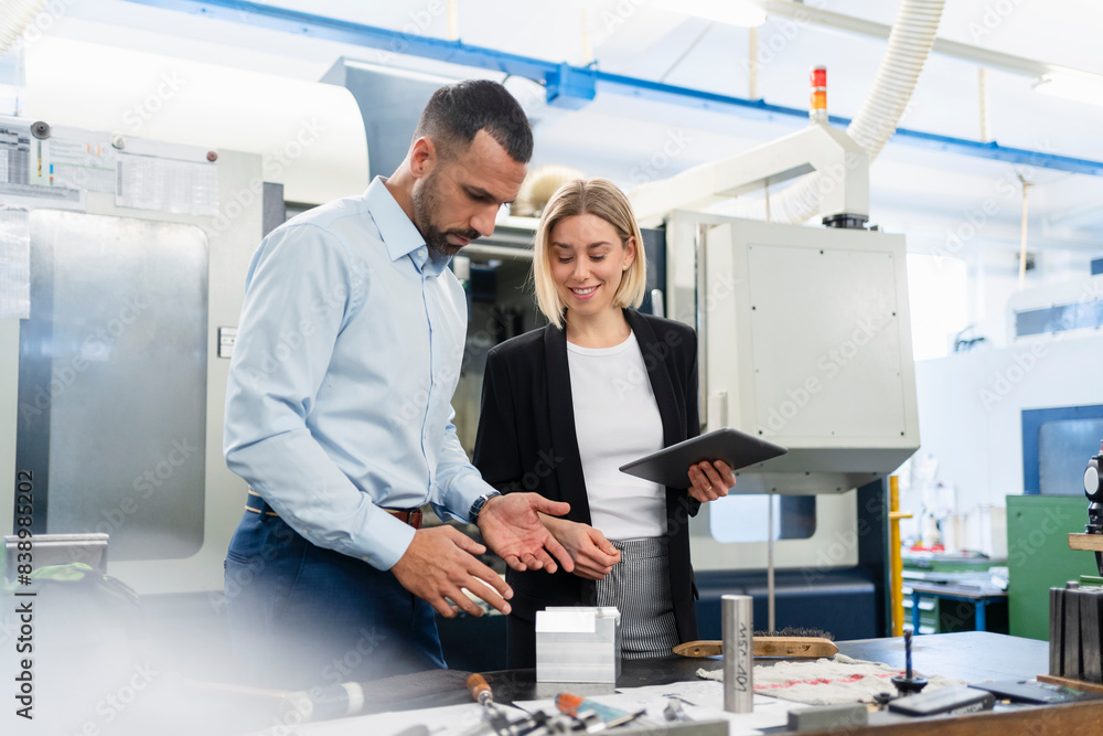 Businessman and woman with tablet and workpiece in factory hall