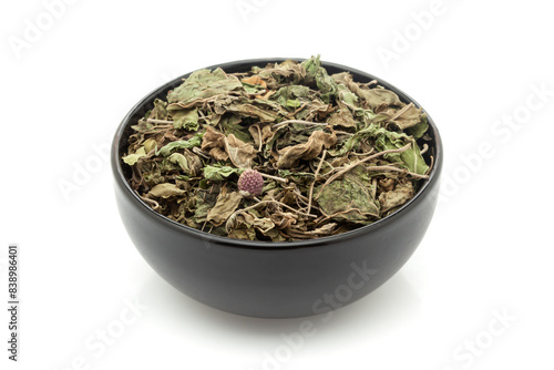 Close-up of Dry Organic Gymnema or Gurmar (Gymnema sylvestre) leaves, in black ceramic bowl. Isolated on a white background. photo