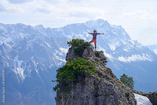 Woman standing with arms outstretched on rocky mountain peak while looking at landscape against sky photo