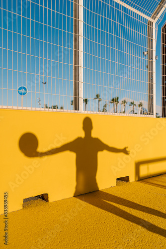Shadow of young man holding basketball on yellow wall in sports court