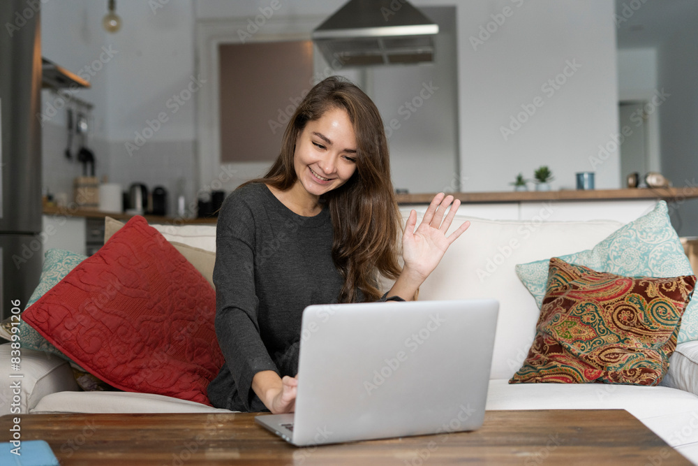 Fototapeta premium Young woman sitting on her couch, chatting on her laptop