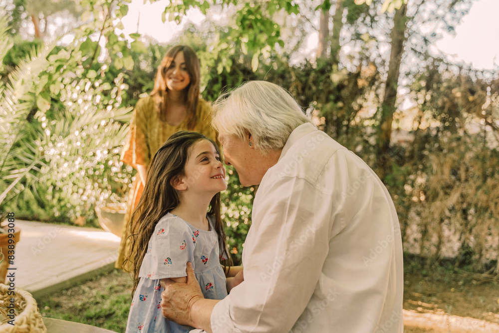 Smiling woman looking at girl playing with grandmother in yard Smiling woman looking at girl playing with grandmother in yard