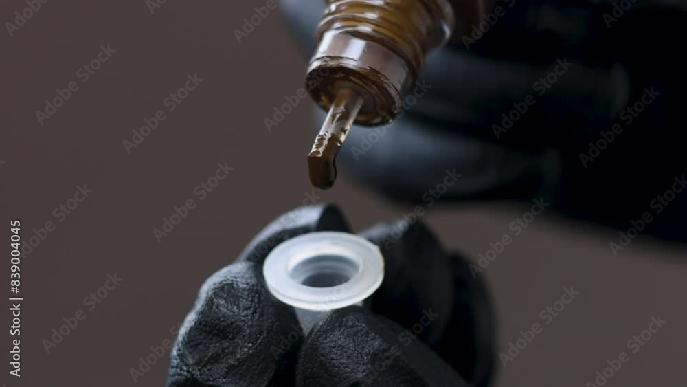 master permanent makeup attaching micro needle on tattoo machine or putting brown and red pigment in mini cup.woman in black or pink gloves, dark background.pen for micropigmentation.