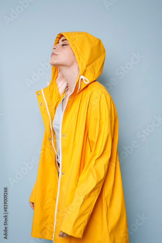 Young woman wearing yellow rain coat in front of blue background photo