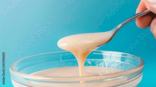 Condensed milk glass and spoon dripping with the sweetened condensed milk photo