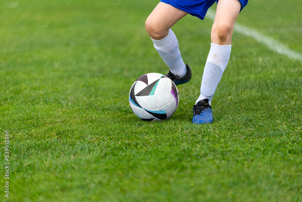 Young soccer player's kick ball. Ball and legs in sharp focus on a lush green field close-up Young soccer player's kick ball. Ball and legs in sharp focus on a lush green field close-up