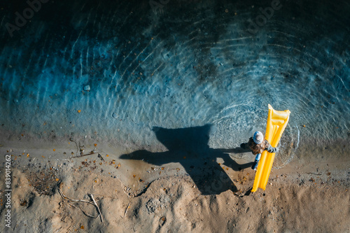 Girl with wooly hat, standing at lakeshore, carrying airbed