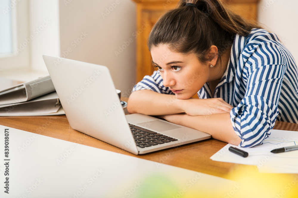 Young woman looking at laptop on desk at home Young woman looking at laptop on desk at home
