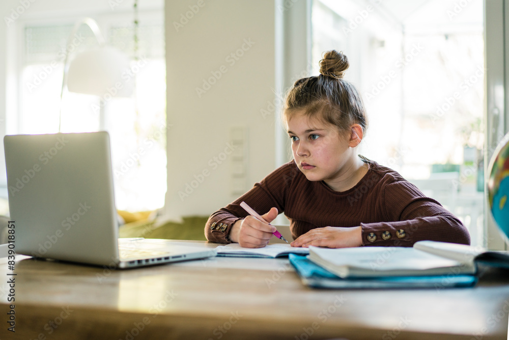 Girl writing in book while studying through laptop at home Girl writing in book while studying through laptop at home