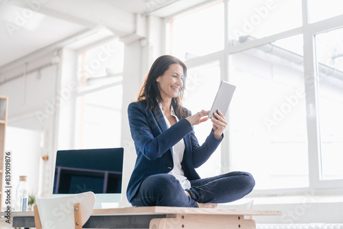 Businesswoman sitting on desk in a loft using tablet © tunedin