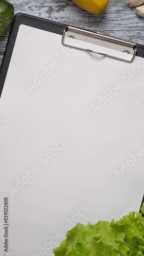 Cook taking lettuce from table with blank paper clipboard placed on wooden table with mixed vegetables. Easy to place Your reciepe on a blank paper. Vertical shot. photo