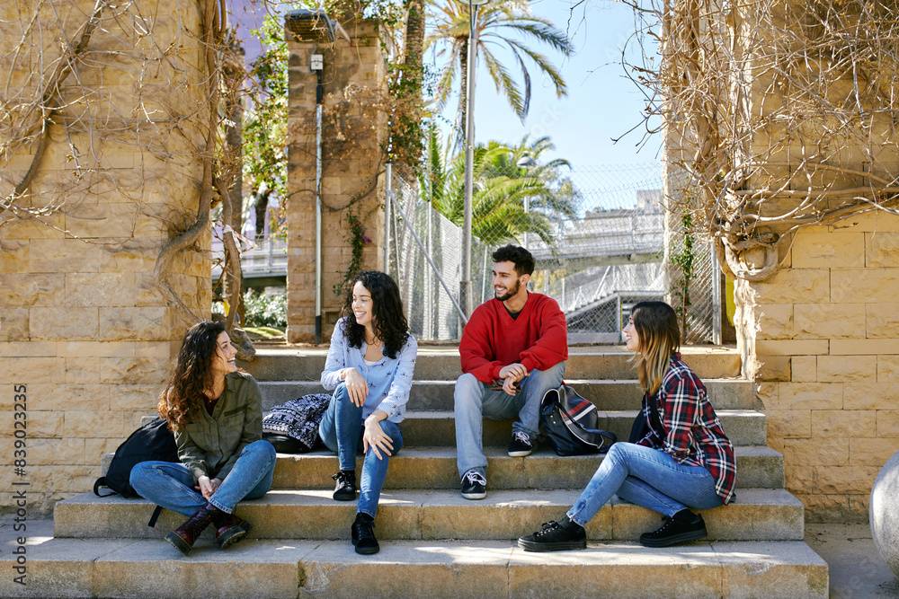 Four happy friends sitting on stairs outdoors talking