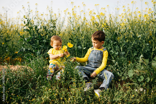 Photography Little boy and baby girl sitting on a meadow with bunch of picked flowers