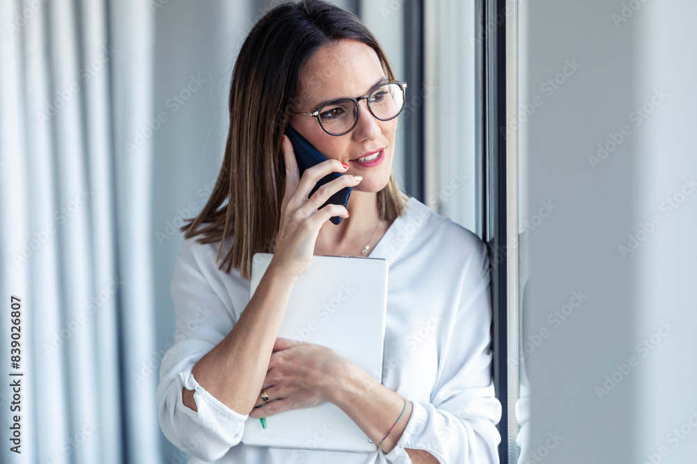 Female entrepreneur phoning and looking out of the window in office Female entrepreneur phoning and looking out of the window in office