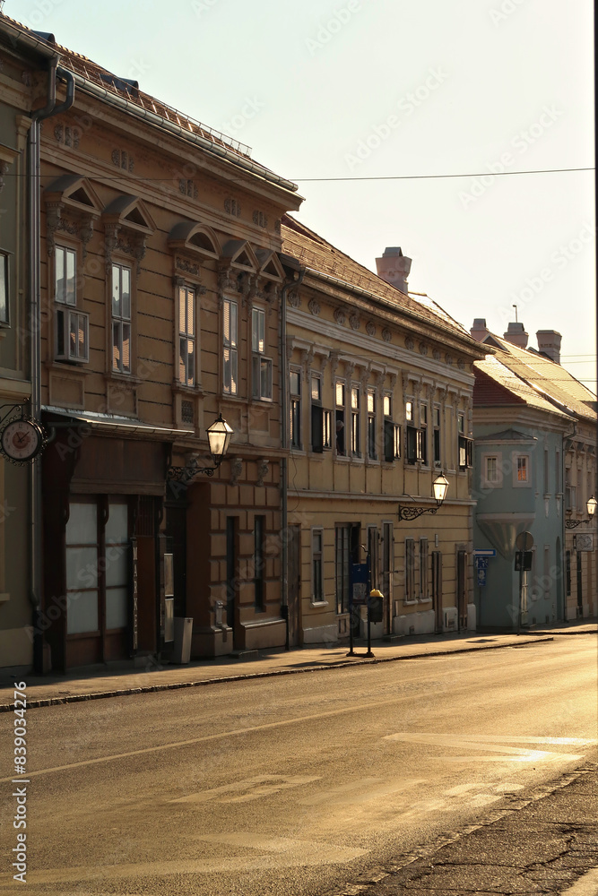 Fototapeta premium Golden hour inside the Petrovaradin Lower Fortress, sunlight is shining through the street lamps, lanterns on the facades of historic buildings and reflecting on the windows, Novi Sad, Serbia