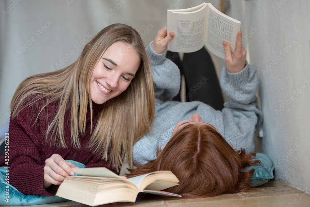 Two friends lying side by side on the floor reading books
