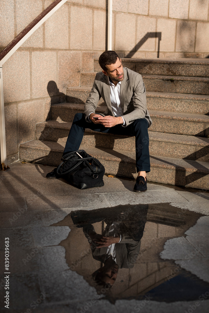 Businessman with bag sitting on stairs using cell phone Businessman with bag sitting on stairs using cell phone