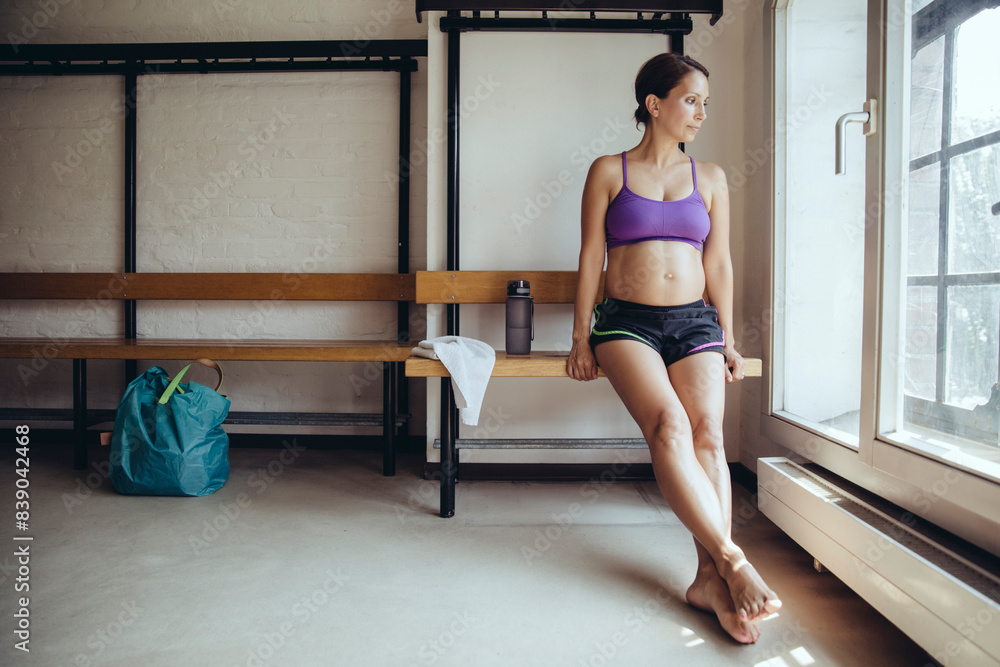 Naklejka premium Sporty pregnant woman sitting in locker room looking out of window