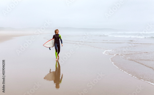 Spain, Aviles, young surfer carrying surfboard on the beach