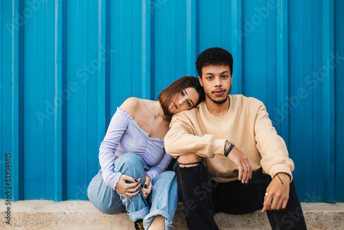 Girlfriend leaning on boyfriend's shoulder while sitting against blue wall