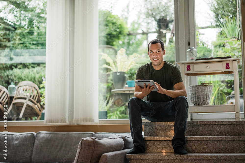 Portrait of smiling man at home sitting on stairs using tablet Portrait of smiling man at home sitting on stairs using tablet
