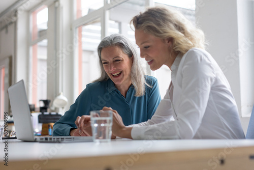 Obraz na płótnie Two happy businesswomen using laptop at desk in office together w salonie