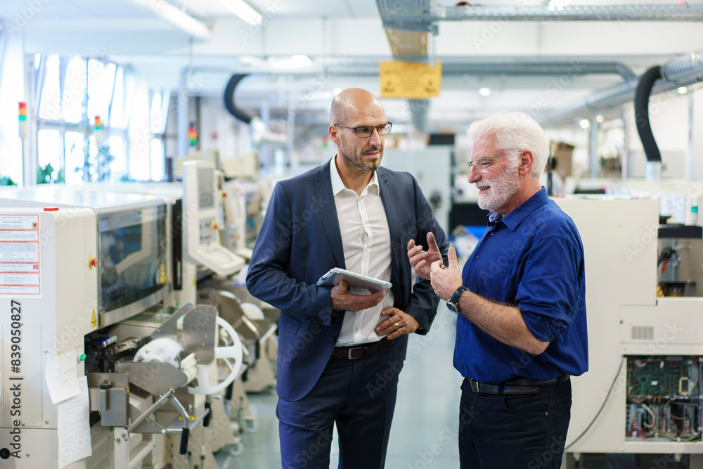 Businessman holding digital tablet while looking at senior manager discussing at illuminated factory
