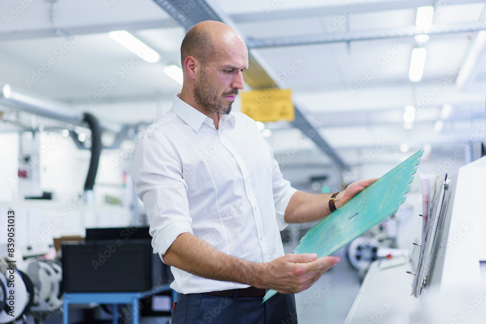 Confident mature male engineer analyzing large circuit board at illuminated factory Confident mature male engineer analyzing large circuit board at illuminated factory