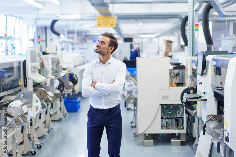 Thoughtful young businessman standing with arms crossed while looking away at illuminated factory Thoughtful young businessman standing with arms crossed while looking away at illuminated factory