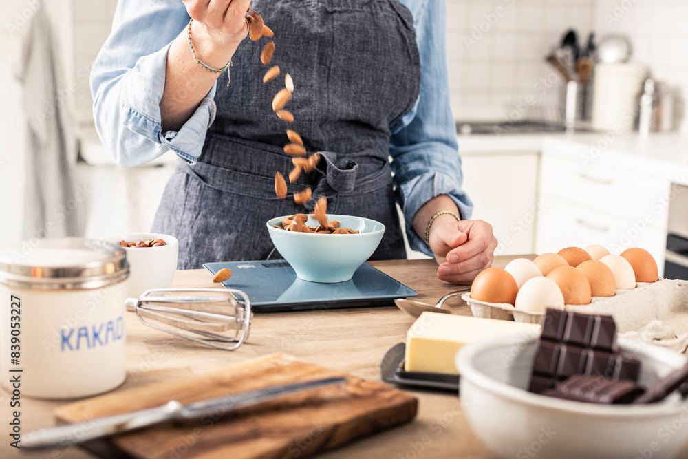 Woman weighing almond on kitchen scale while standing in kitchen at home Woman weighing almond on kitchen scale while standing in kitchen at home