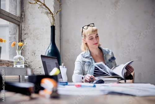 Portrait of smiling woman sitting at desk in a loft leafing through book photo