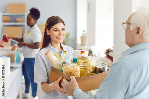 Canvas Print Positive volunteer woman giving a food donation box to a pensioner at a social assistance center or organization