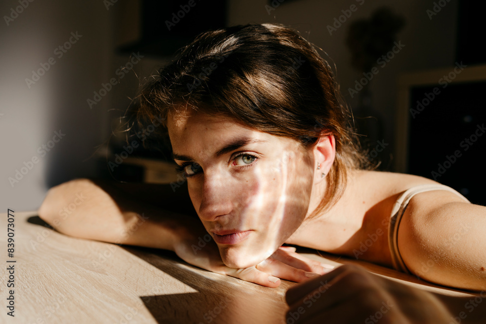 Naklejka premium Portrait of young woman leaning on wooden table at sunlight