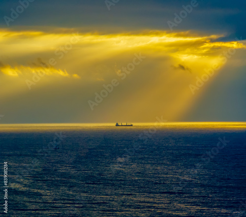 Sunrise Seascape with sunrays in the cloud covered sky and ship on the horizon photo