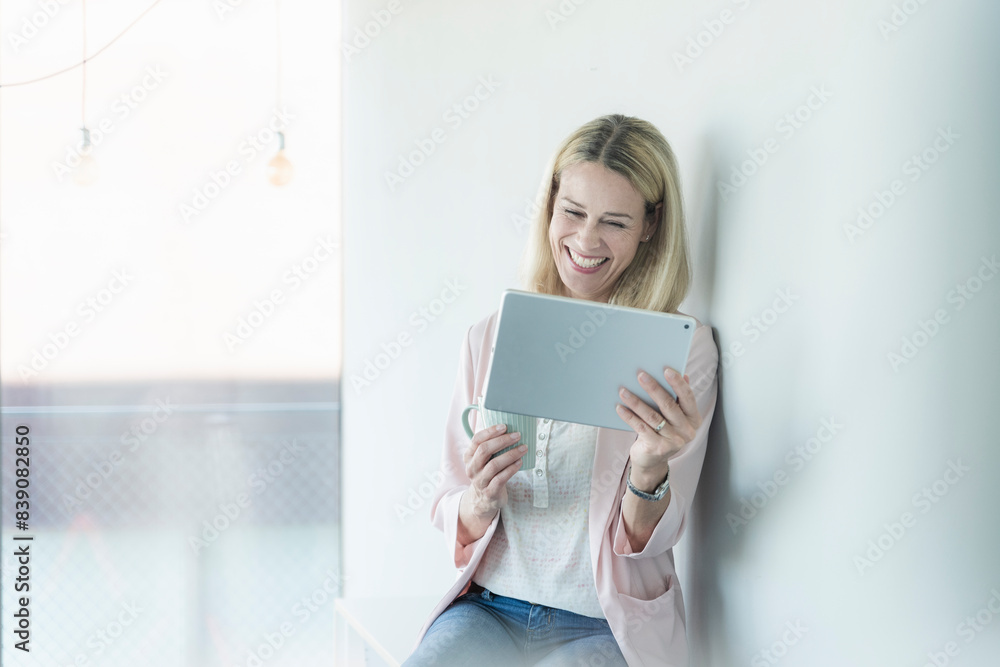 Happy businesswoman leaning against a wall using tablet Happy businesswoman leaning against a wall using tablet