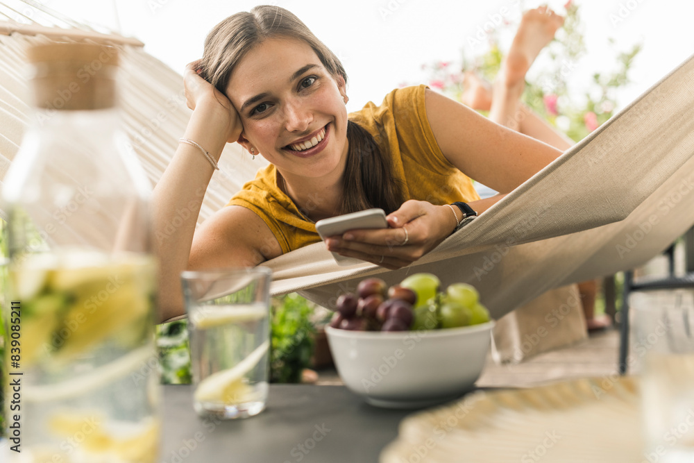 Smiling beautiful woman using smart phone while resting on hammock