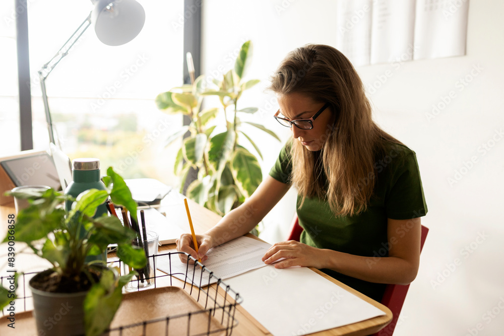 Businesswoman writing on paper while sitting in home office Businesswoman writing on paper while sitting in home office