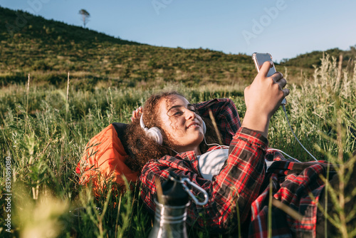 Obraz na płótnie Teenage girl with backpack lying on a meadow listening music with headphones and cell phone w salonie