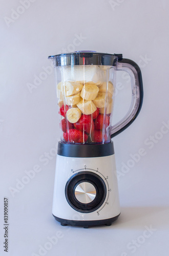 White mixer with fruits and berries, banana, strawberry on gray background photo