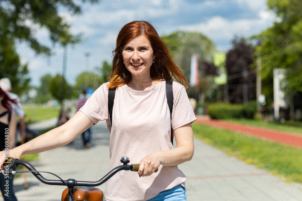 Obraz premium Pretty Woman walking and holding her bike next to her in the park 
