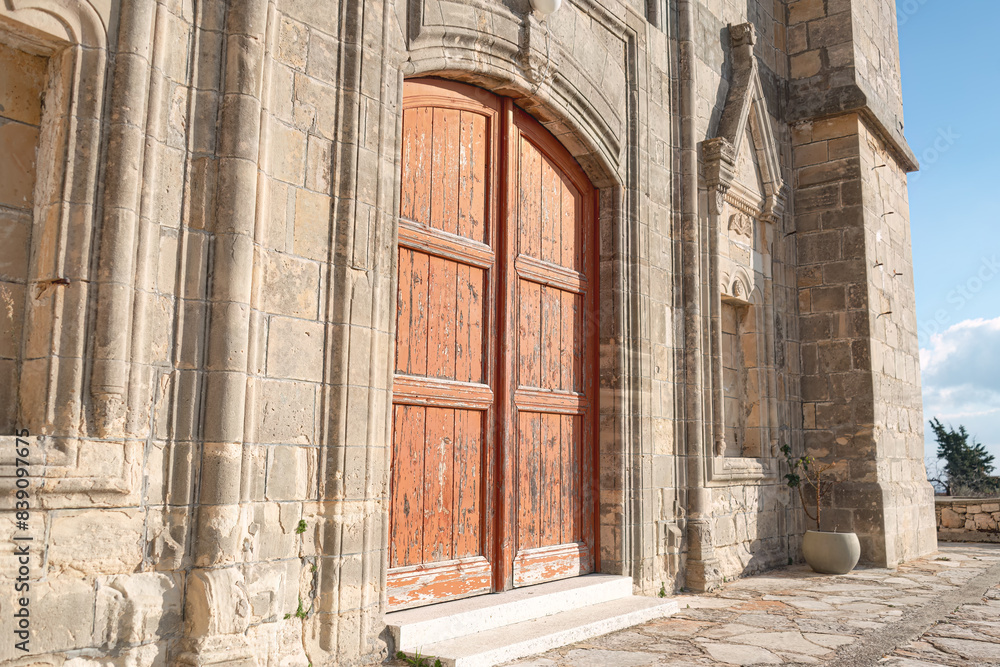Fototapeta premium Old wooden door on a weathered stone Church of Timios Prodromos facade at Vouni village. Limassol District, Cyprus