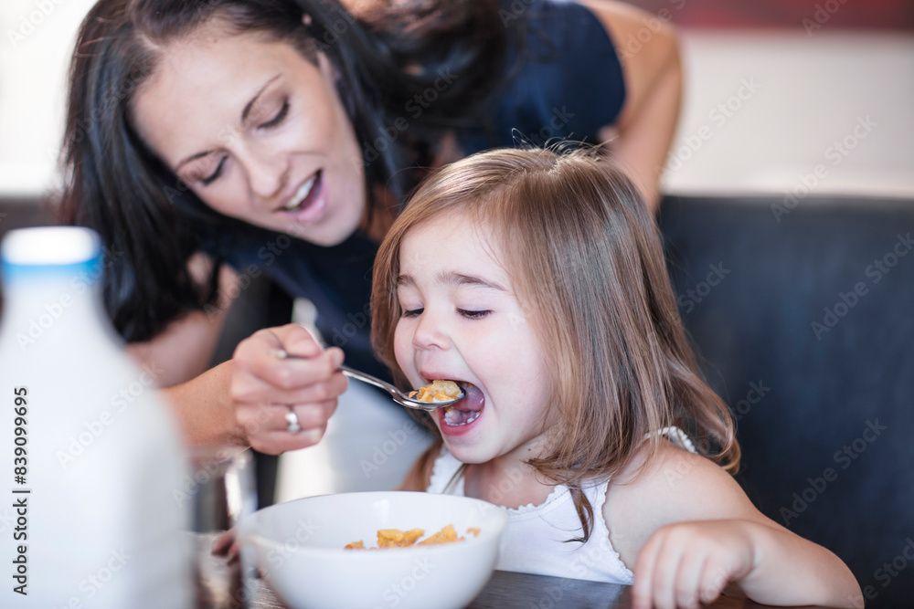 Mother feeding daughter breakfast cereal at table Mother feeding daughter breakfast cereal at table