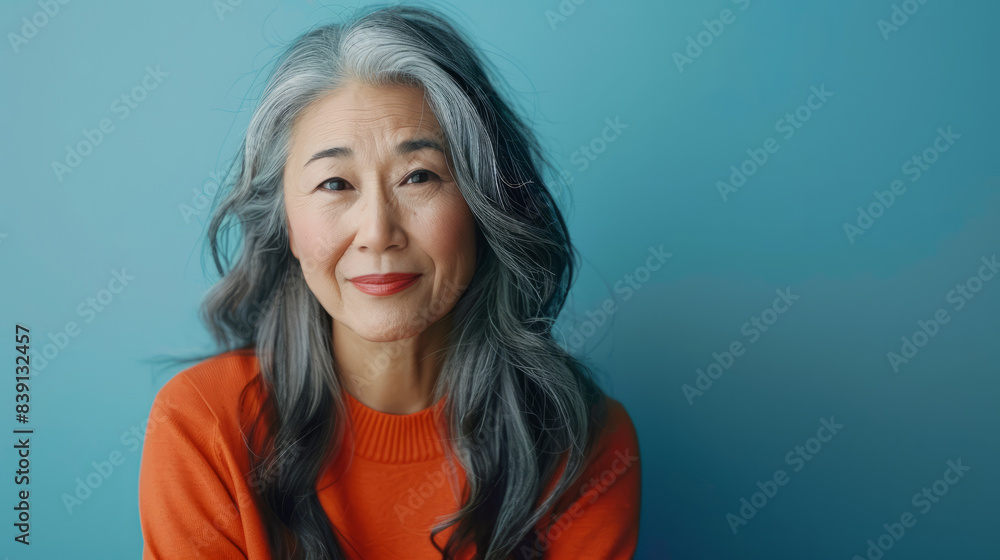 Senior Asian woman with long grey hair smiling, wearing an orange sweater on a blue background Senior Asian woman with long grey hair smiling, wearing an orange sweater on a blue background